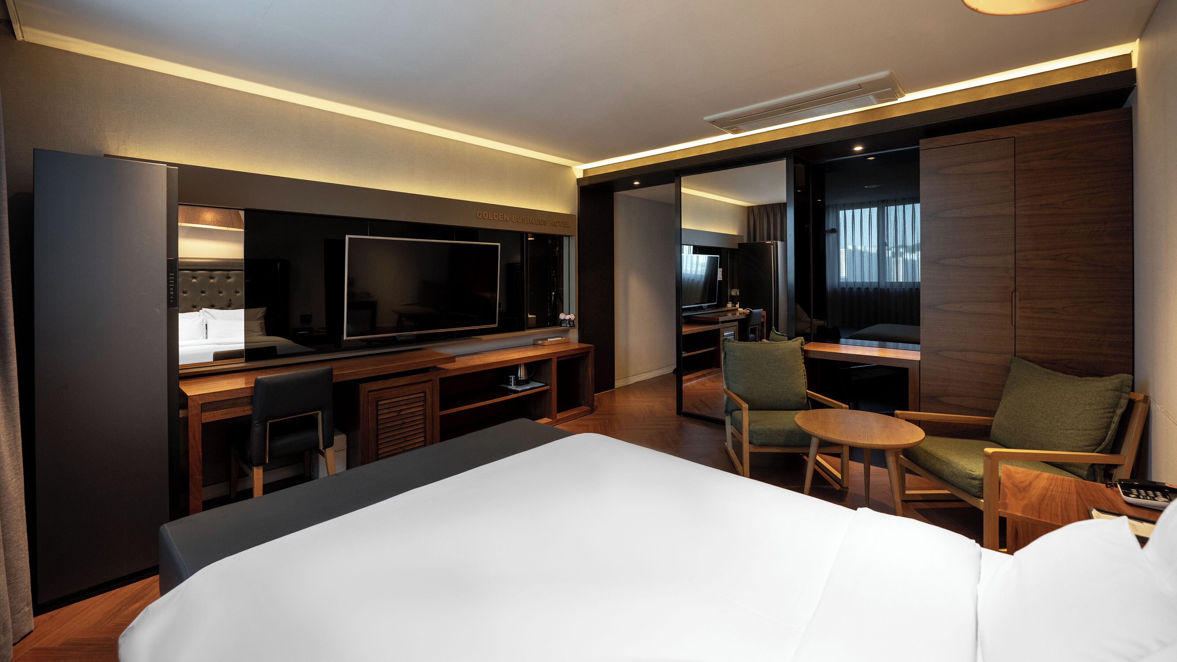 A hotel room with a large bed, a TV, a desk with a computer, and a seating area with chairs and a table.