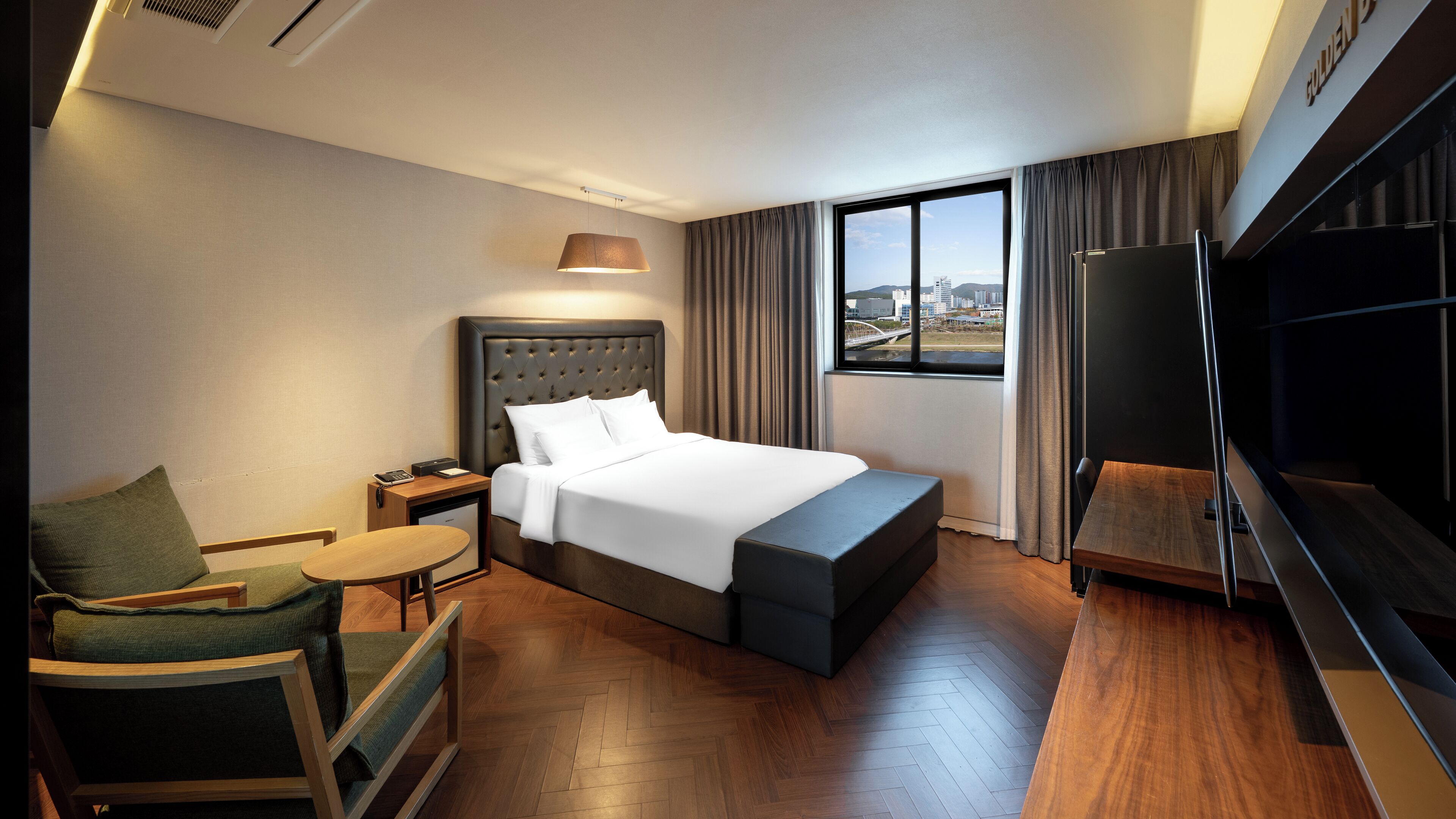 A hotel room with a bed, a desk, a chair, a TV, and a large window with a city view.