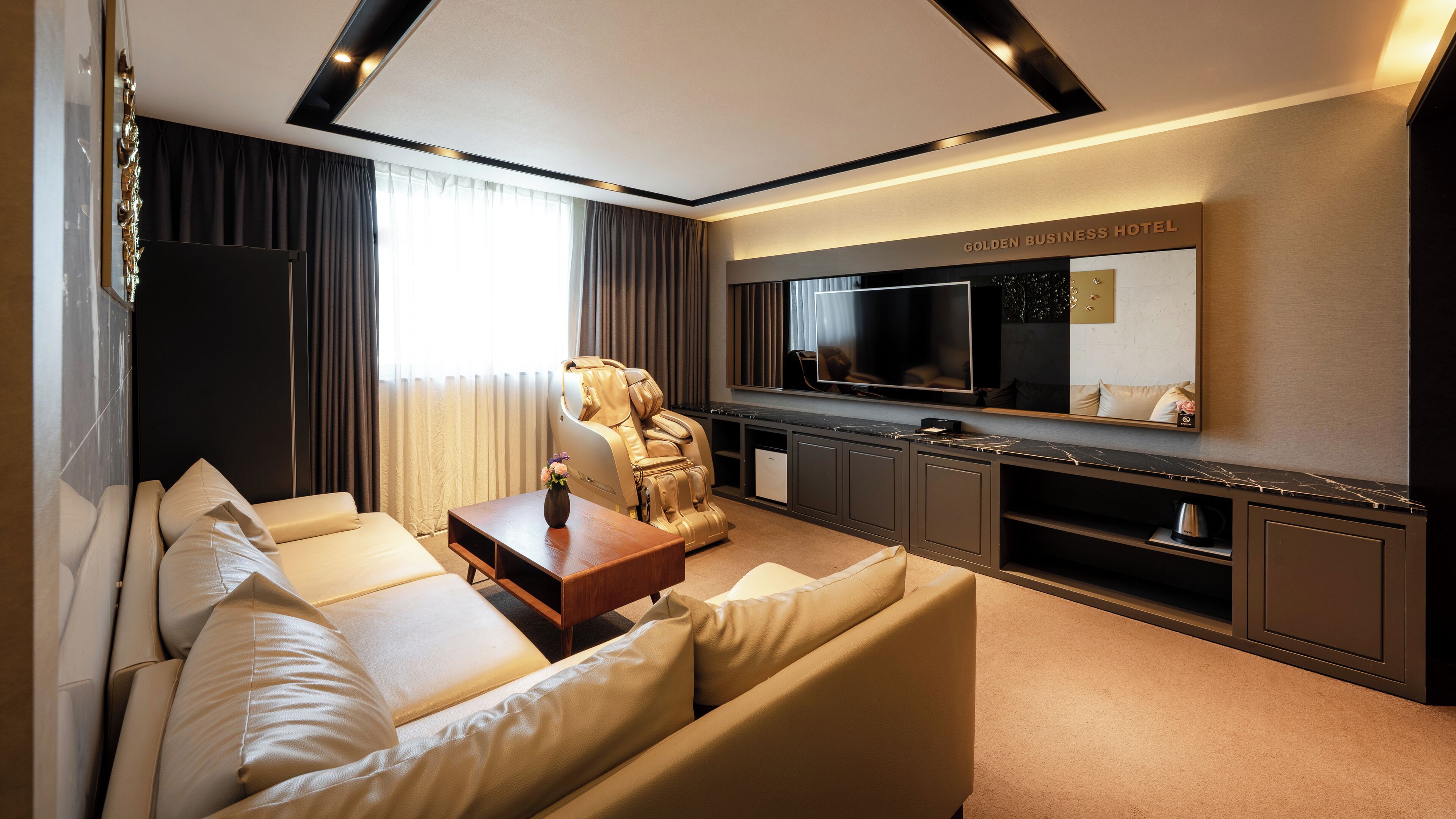 A modern living room with a sofa, a massage chair, a TV, and a minibar.