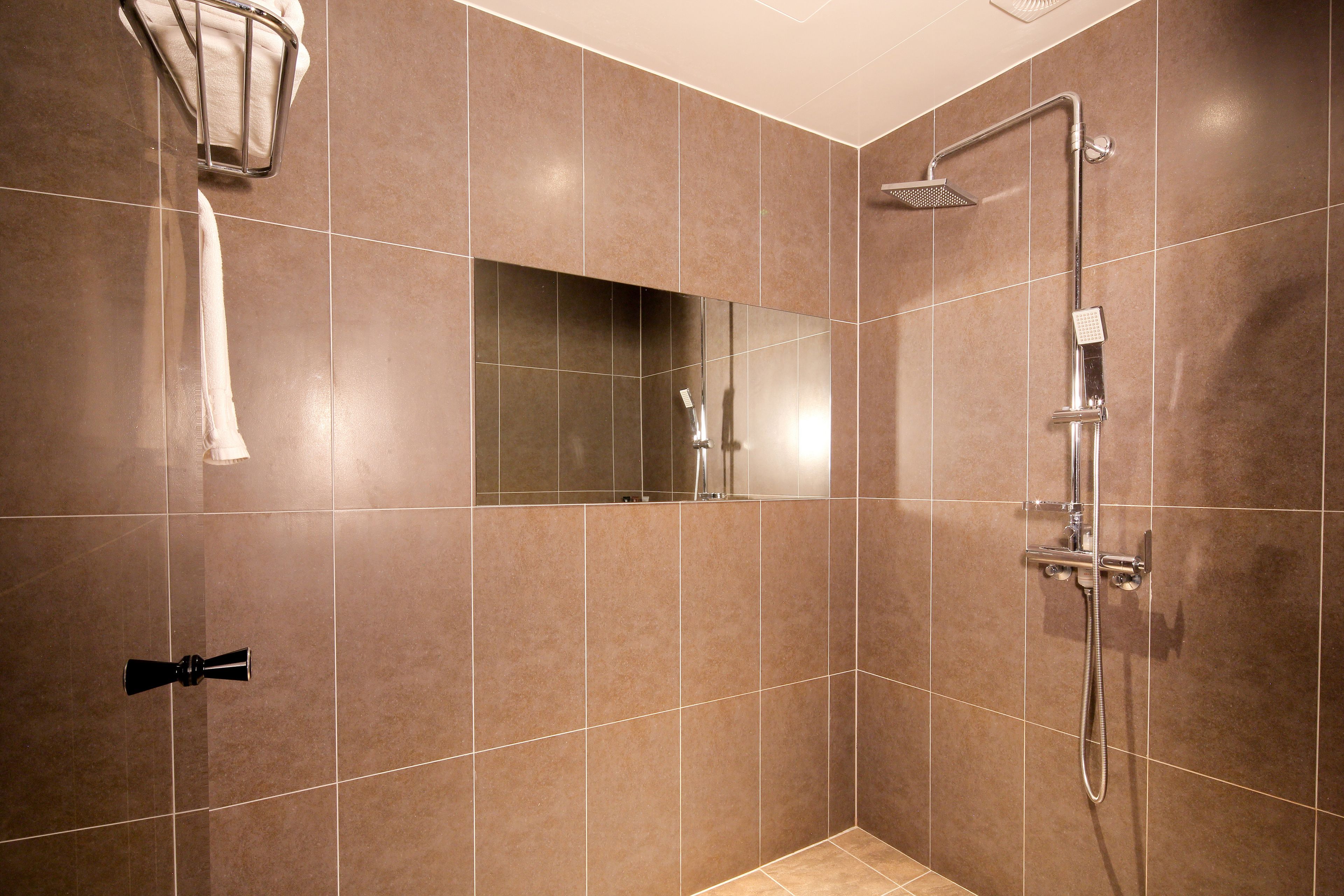 A modern bathroom with a shower, a towel rack, and a mirror.