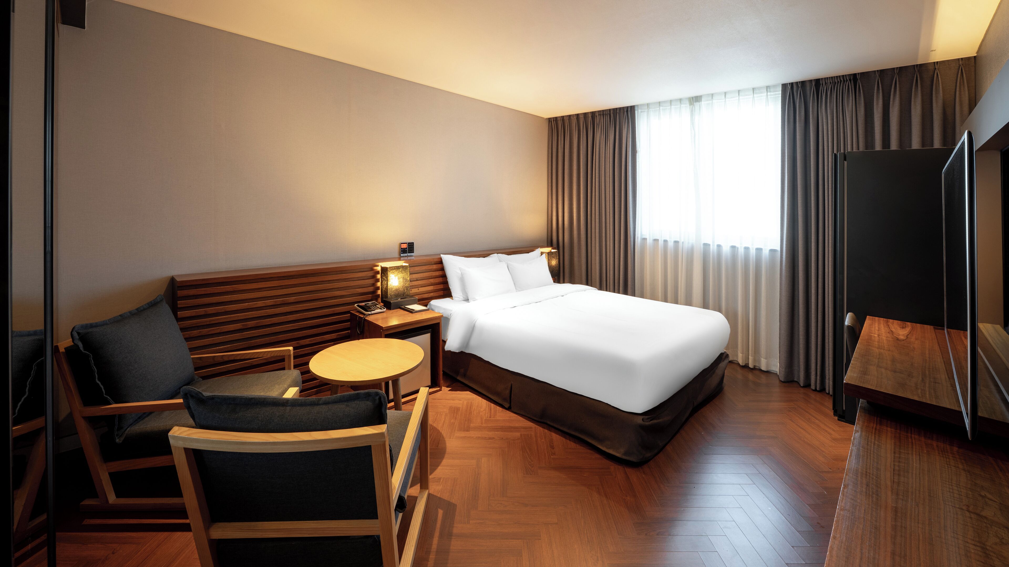 A hotel room with a bed, a desk, a chair, a TV, and a window with curtains.