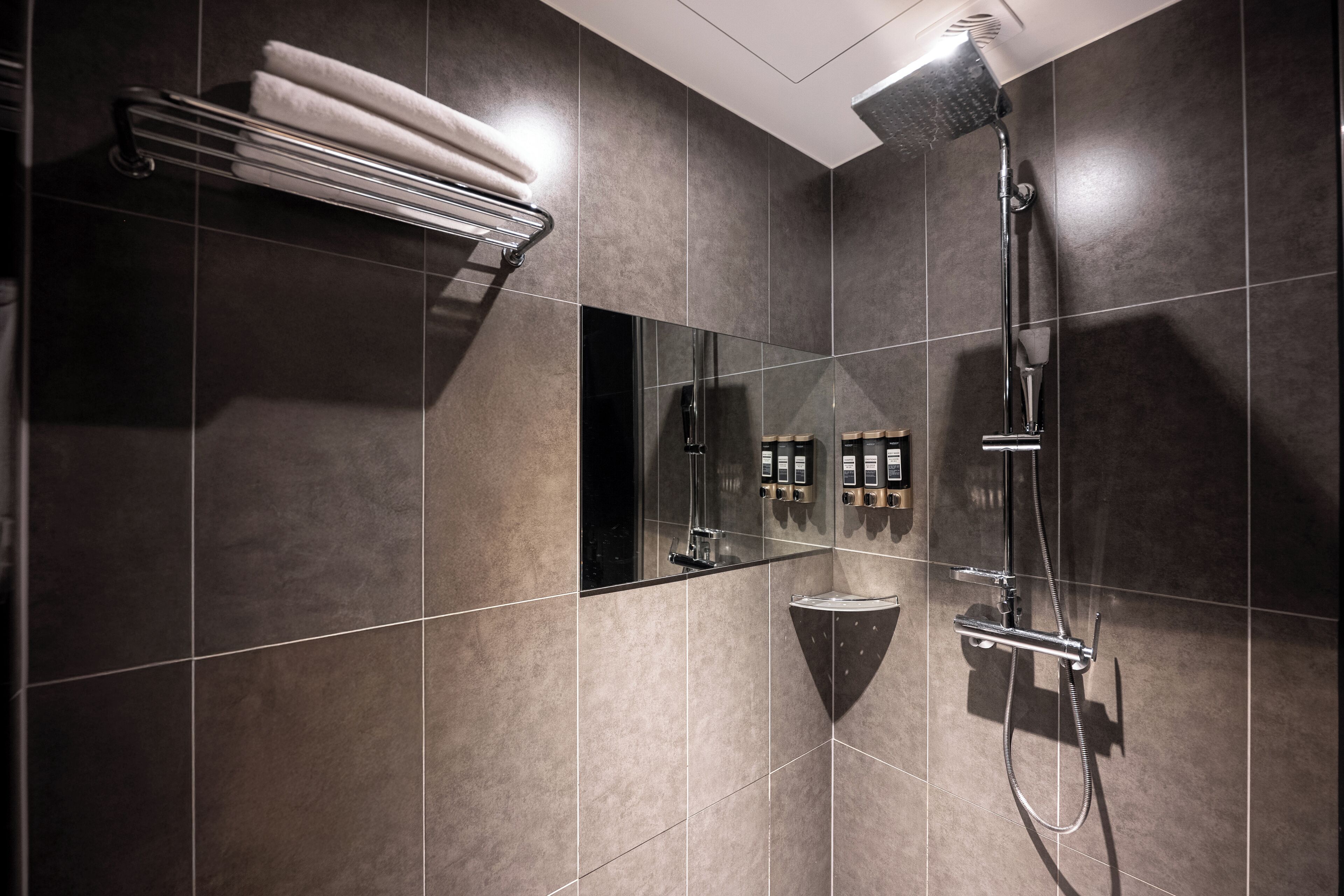 A modern bathroom with dark tiles, a glass-enclosed shower, and a towel rack.