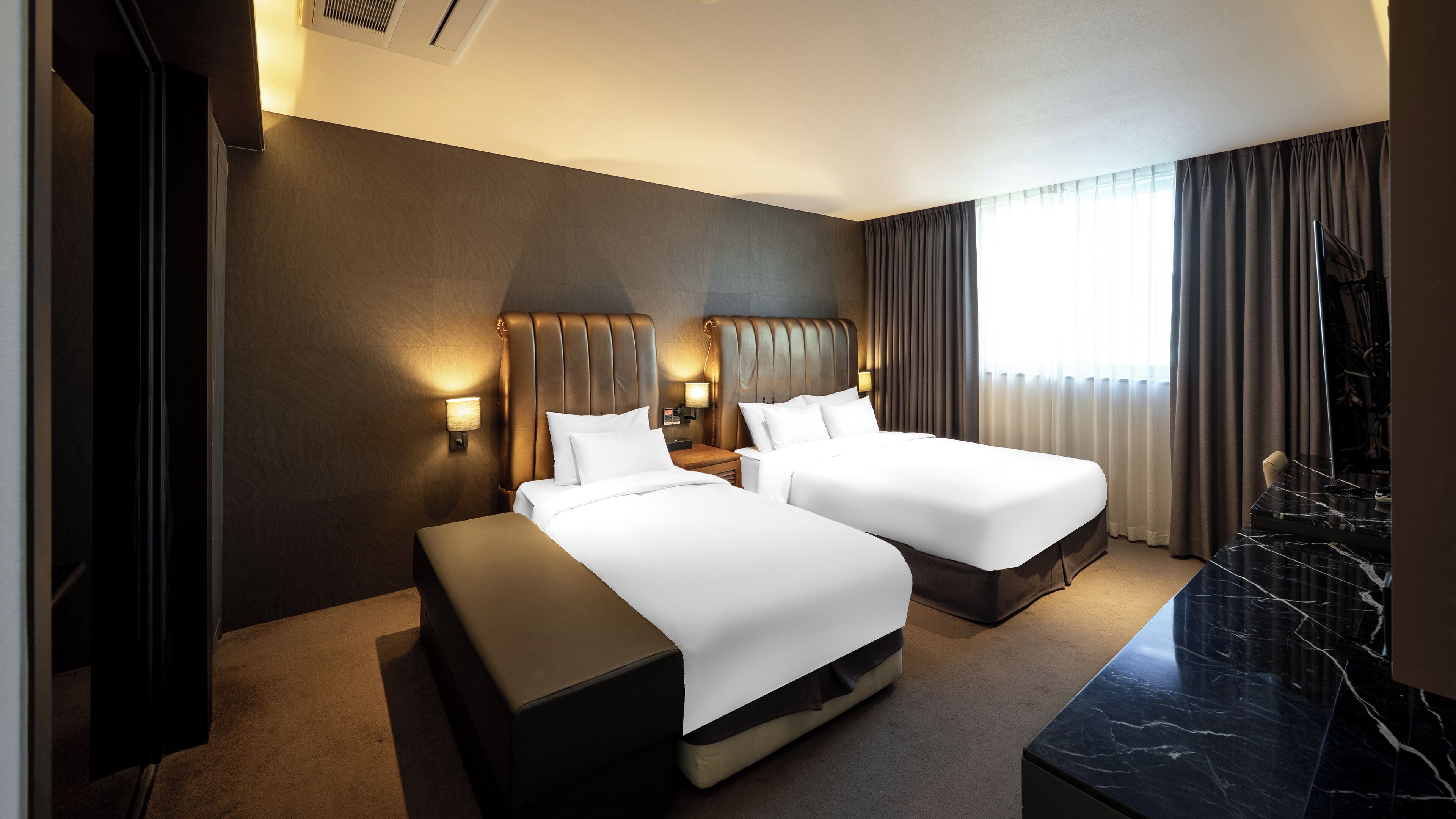 A hotel room with two beds, a marble side table, a TV, and a large window with curtains.
