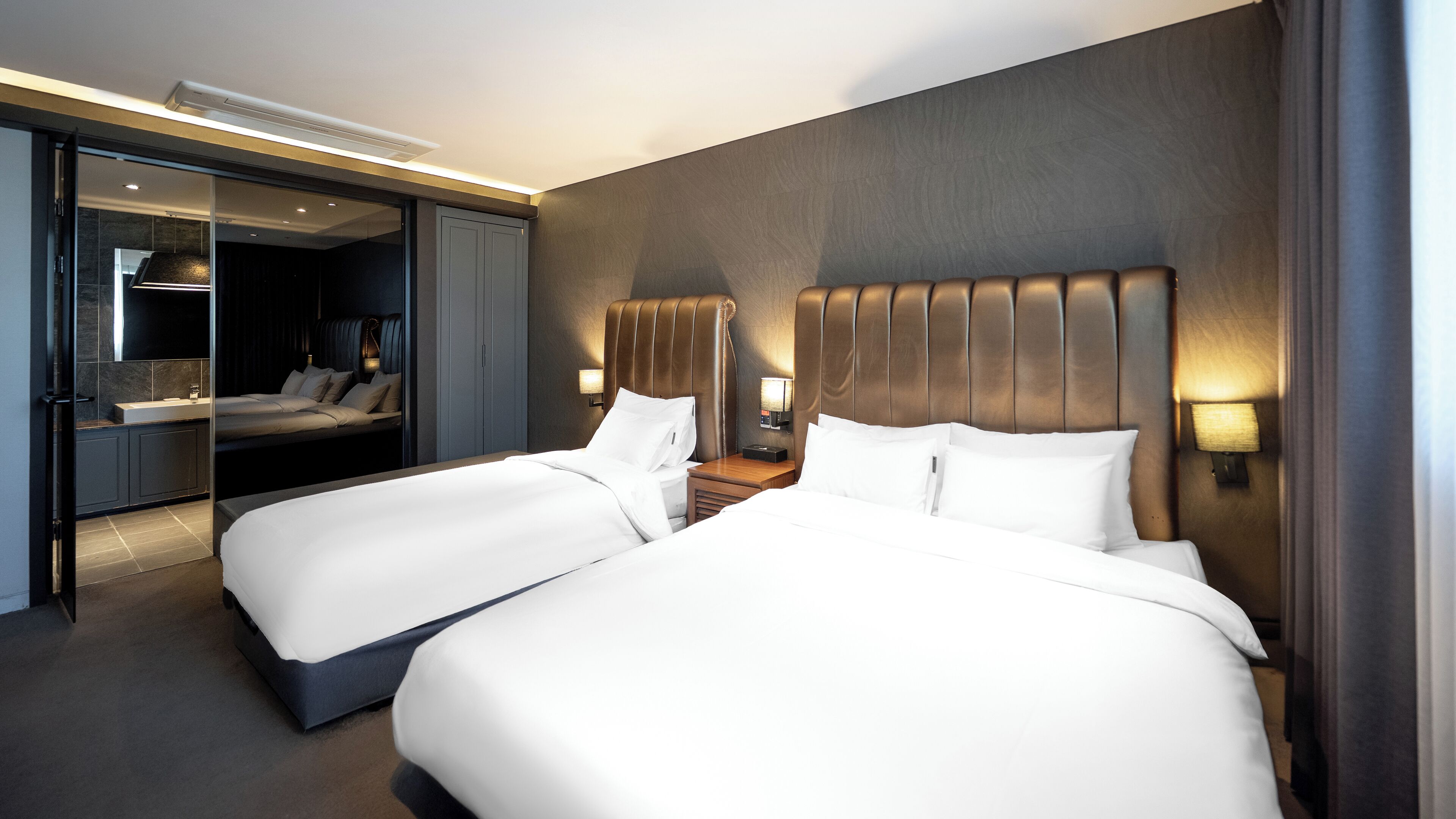 A hotel room with two large beds, a mirror, a vanity, and a walk-in closet.