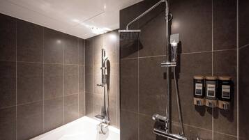Un baño moderno con bañera, ducha con cabezal de ducha de mano y dispensadores de jabón de pared.