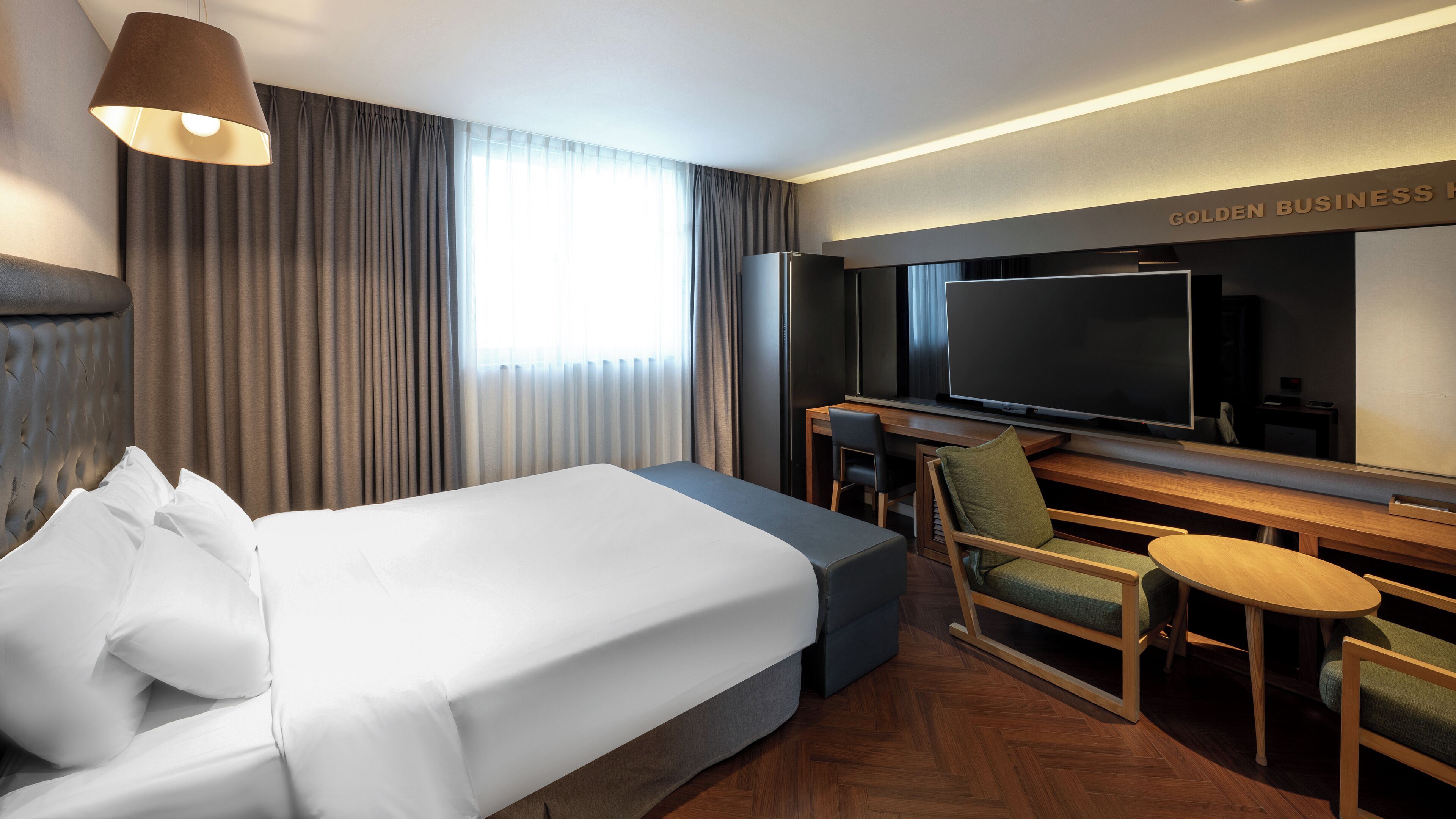 A hotel room with a large bed, a desk with a television, and a seating area with chairs and a small table.