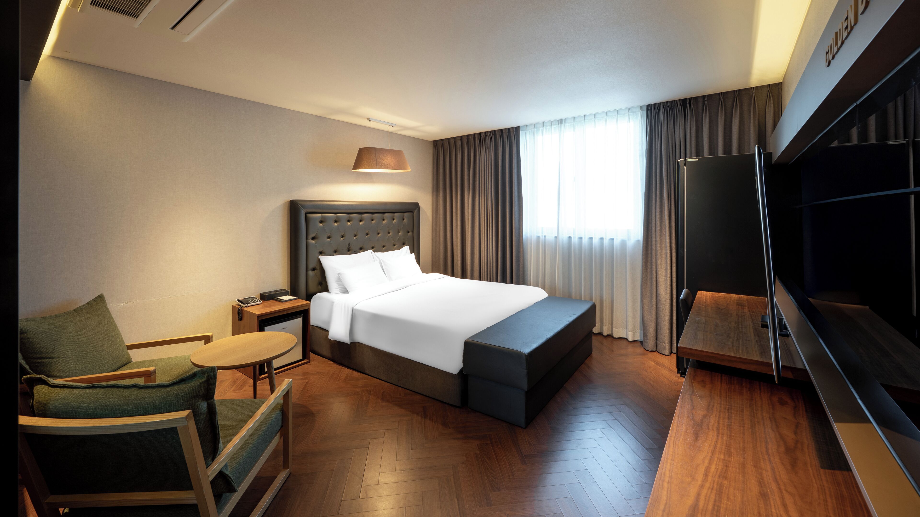Habitación de hotel con una cama grande, un escritorio, una silla, un televisor y una ventana con cortinas.