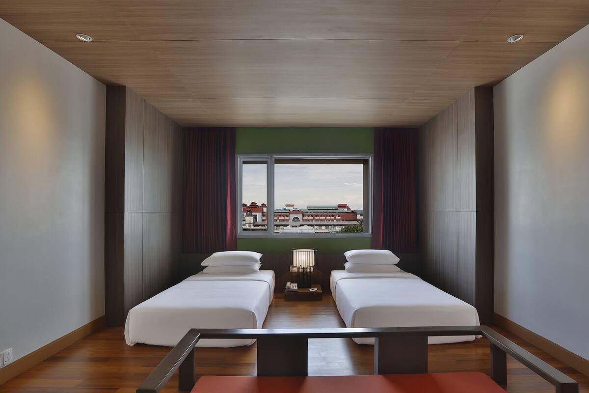 Quarto de hotel com duas camas, vista para a cidade e teto de madeira.