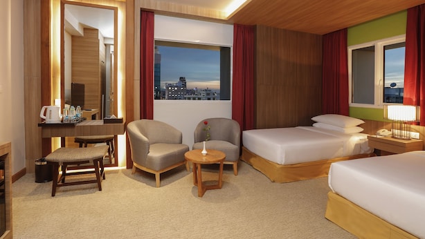 A hotel room with a desk, two armchairs, a small round table with a vase, a bed, and a view of the cityscape. - The Link 83 Mandalay Boutique Hotel (Mandalay)