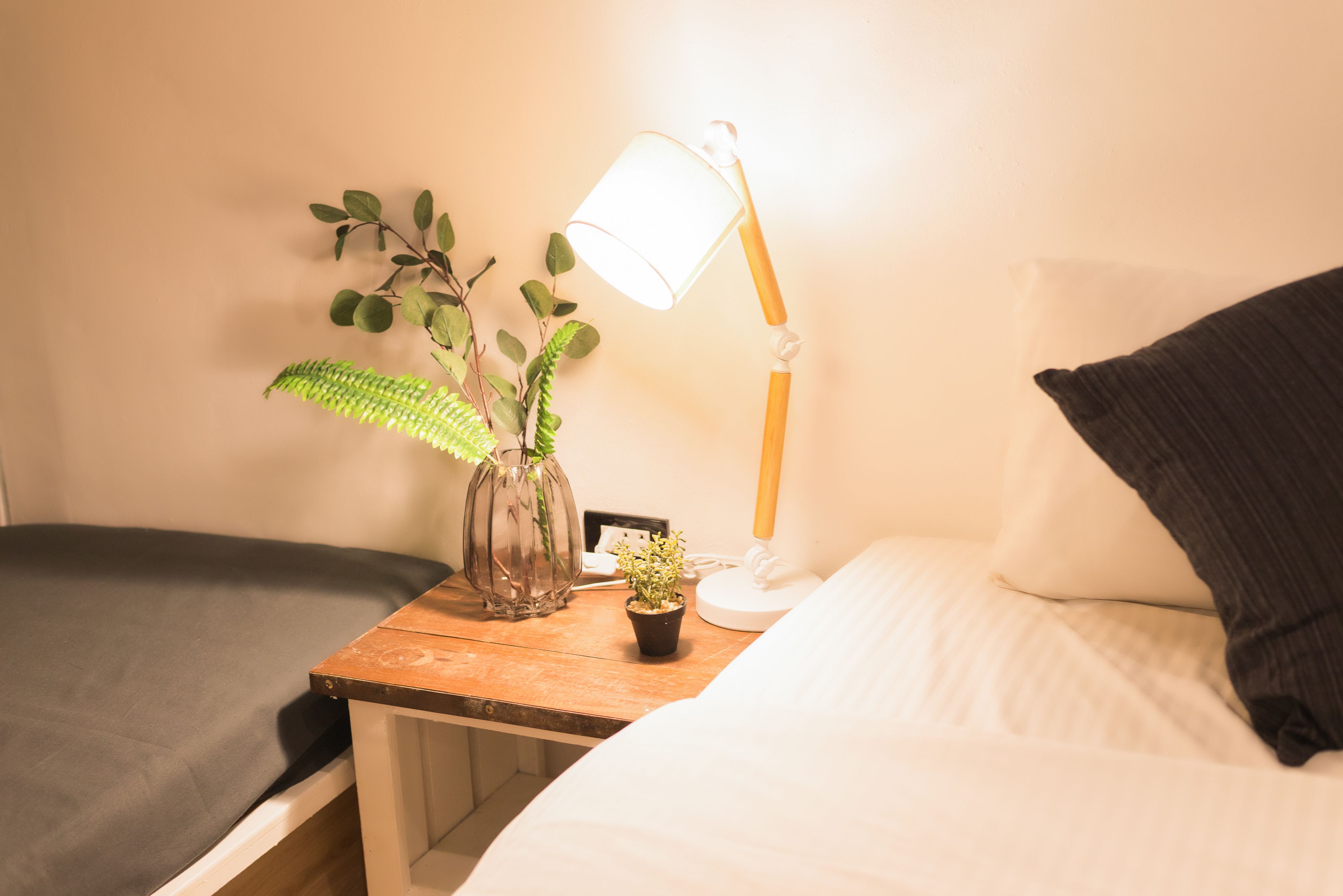 A bedroom with a bed, a bedside table with a lamp, a small potted plant, and a vase with leaves.