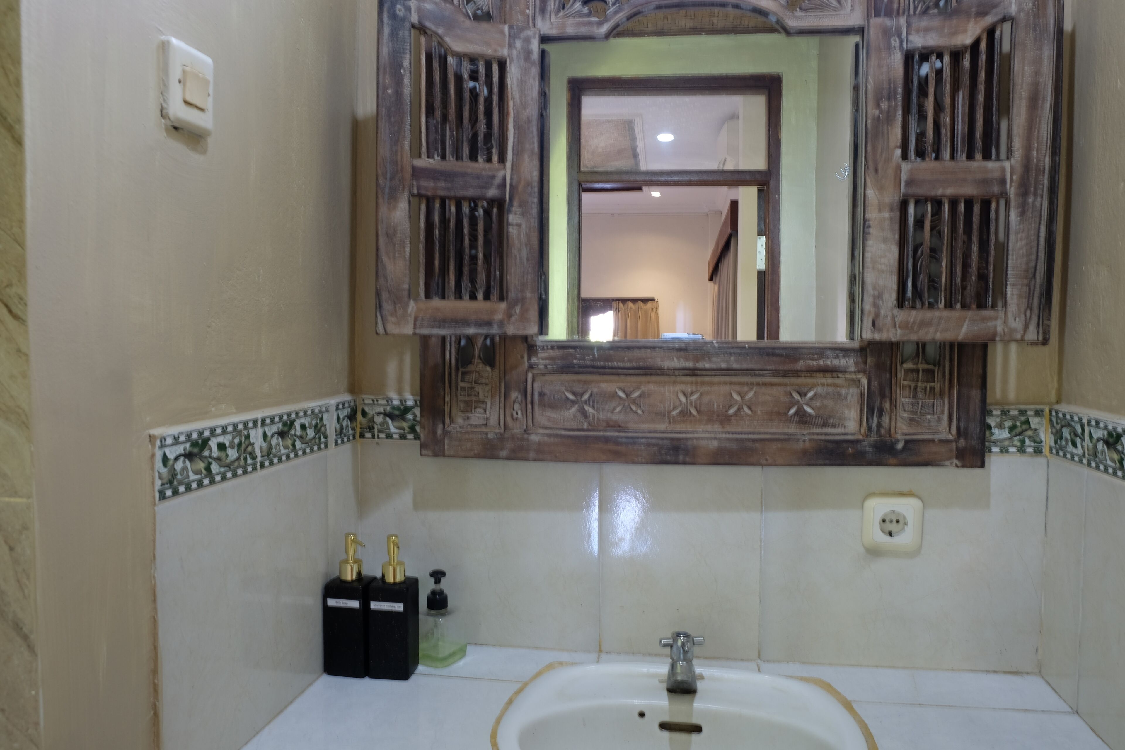 A bathroom with a white sink, a mirror with wooden frames, and a decorative tile border.