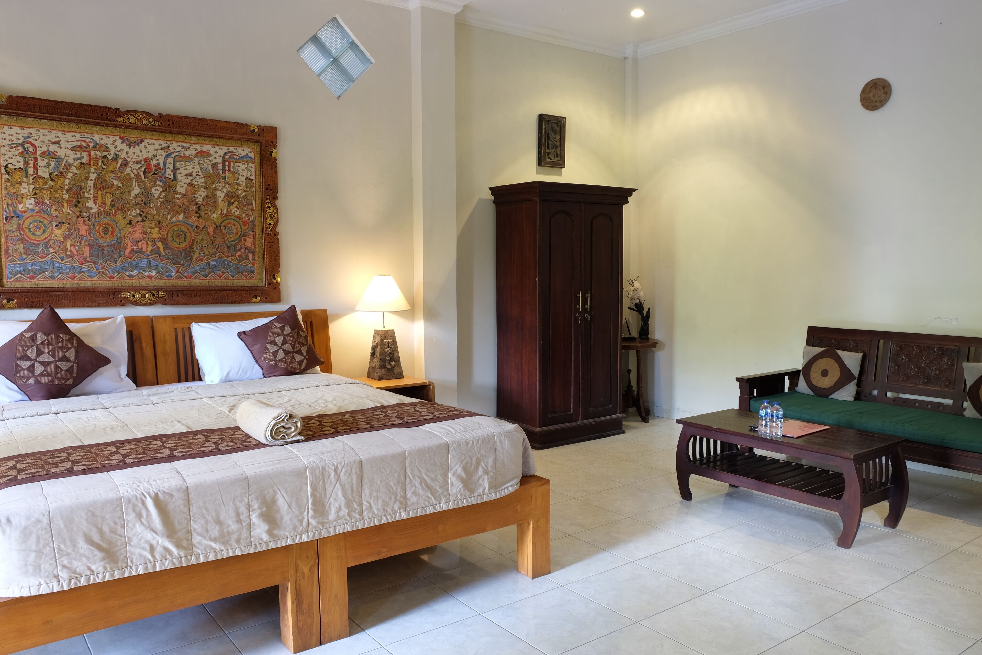 A bedroom with a large bed, a wooden nightstand, a green sofa, a wooden cabinet, and a large tapestry on the wall.
