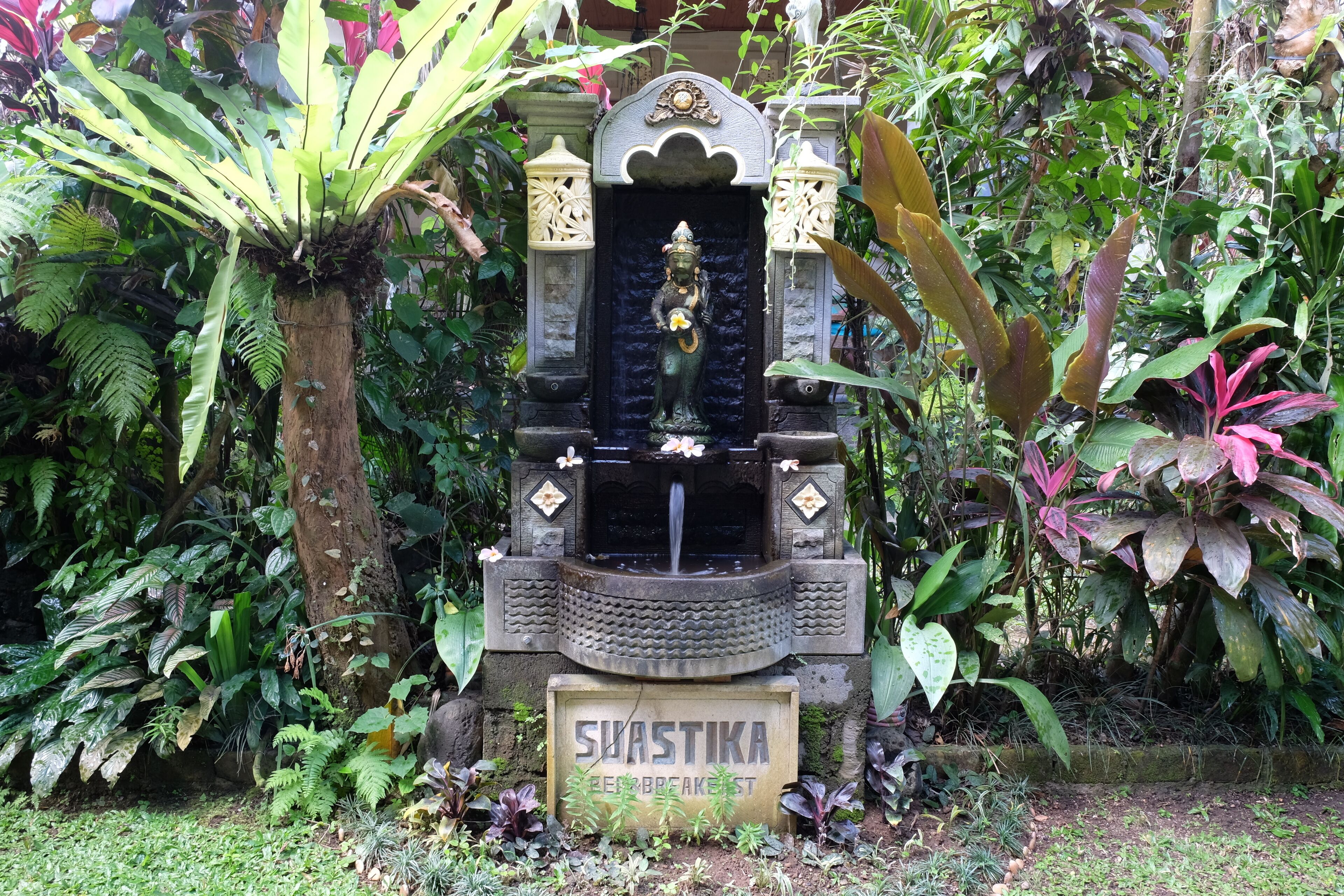 A stone structure with a statue, surrounded by lush greenery.
