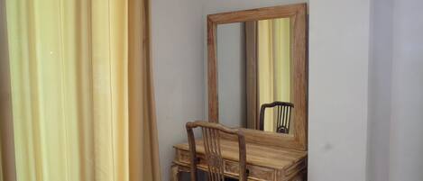 A wooden desk with a mirror, a chair, and a curtain.