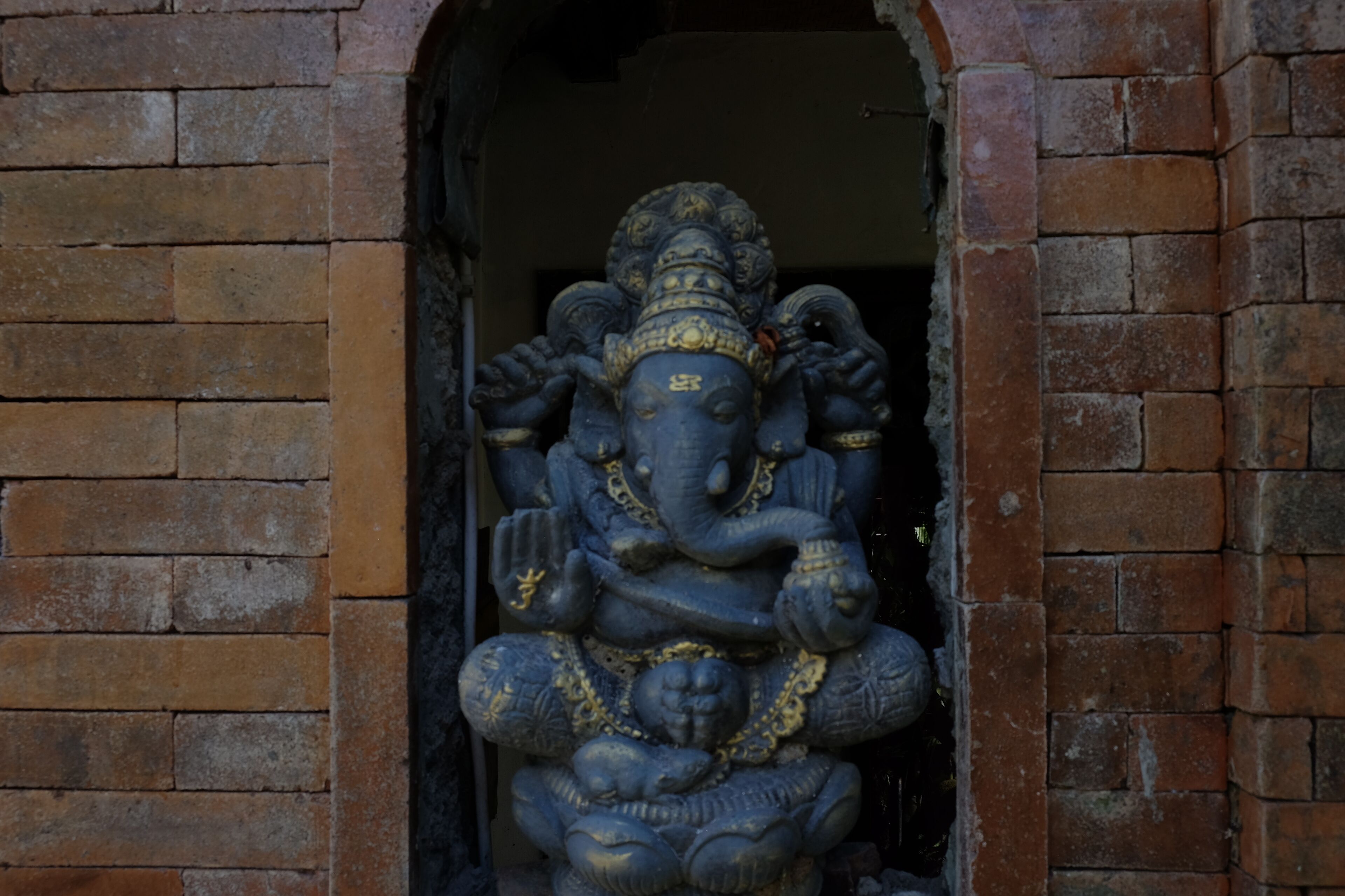 A stone statue of a deity with multiple arms, set in a doorway with brick walls.