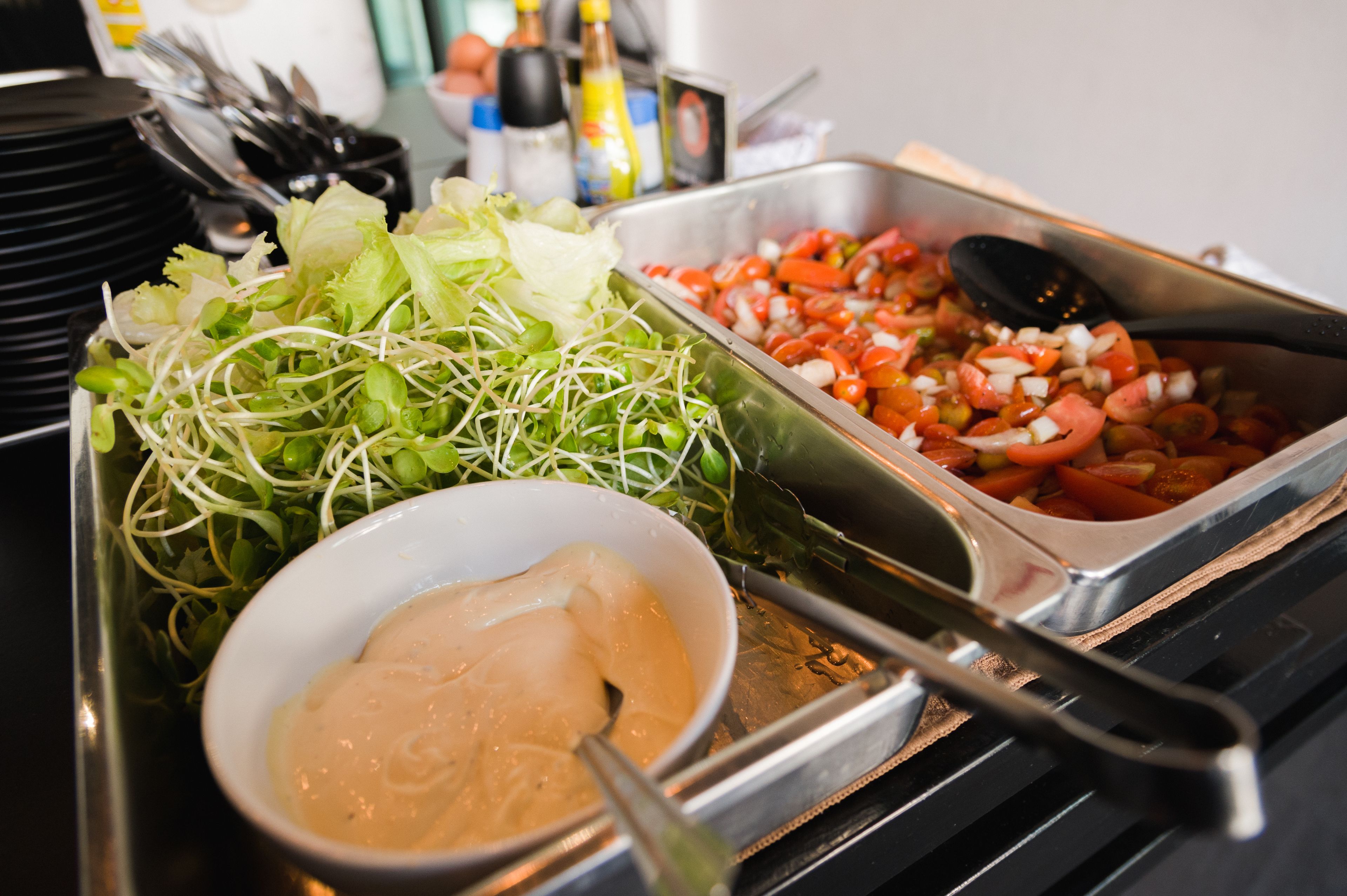 Un bufé con diversos platos, incluyendo una ensalada, un recipiente con salsa y una bandeja de vegetales mixtos.