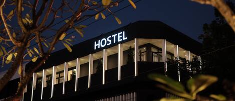A modern hostel with a prominent 'HOSTEL' sign, large windows, and a balcony area.