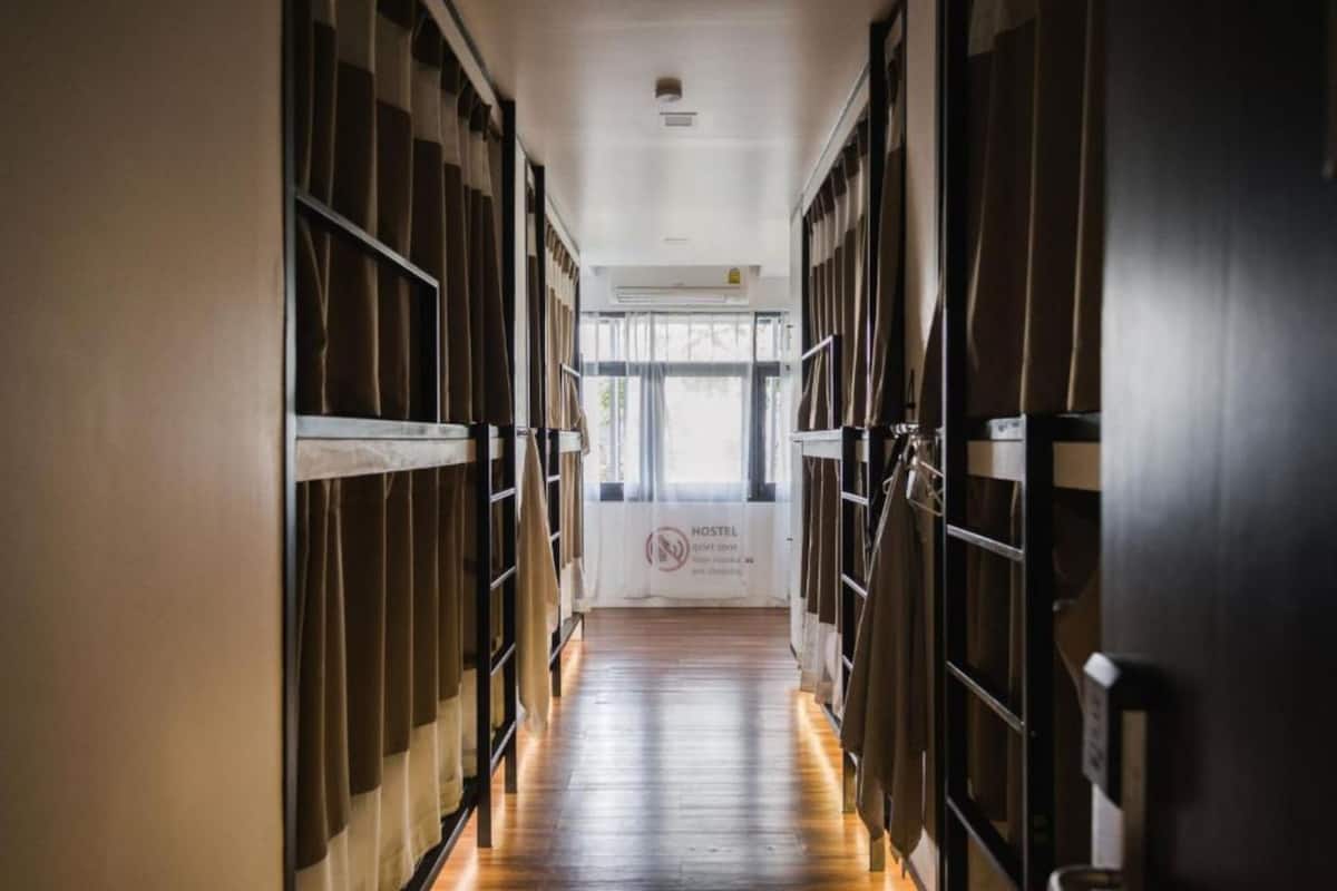 A corridor with bunk beds on either side, leading to a window with a sign that reads "HOSTEL."