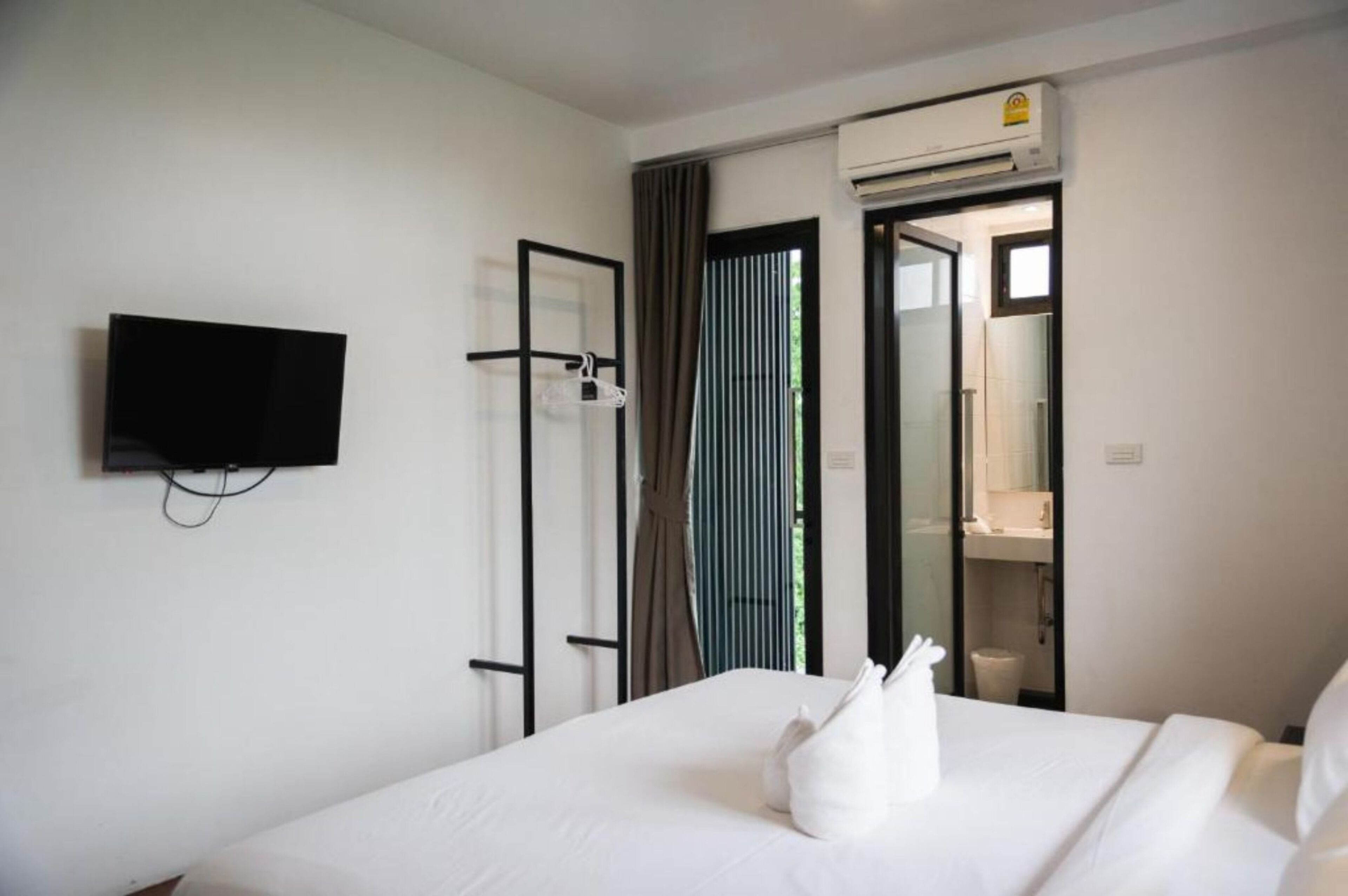 A hotel room with a bed, a television mounted on the wall, a bathroom visible through an open door, and an air conditioning unit on the wall.