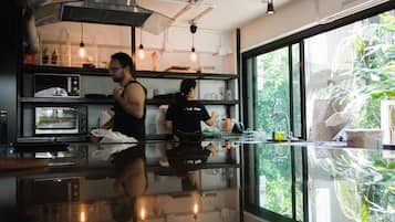 A kitchen with stainless steel appliances, a glass countertop, and a view of greenery through large windows.