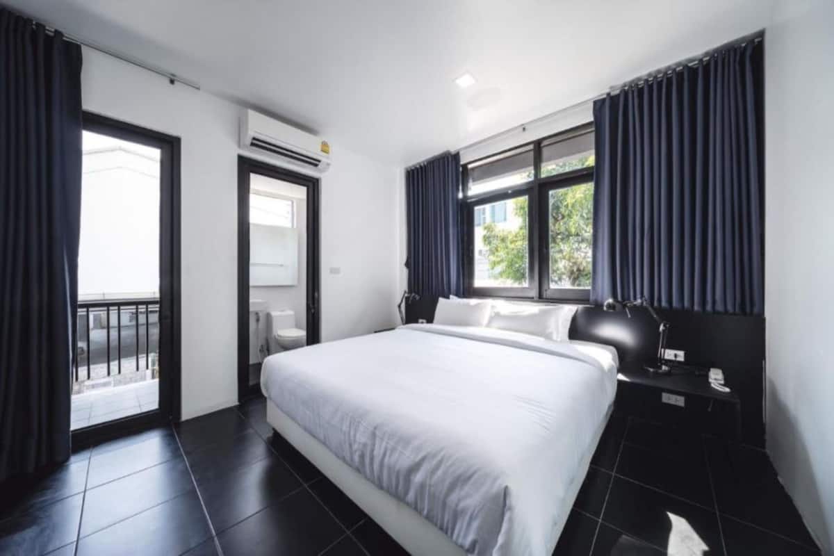 A modern hotel room with a large bed, a nightstand, a desk lamp, and a window with curtains.