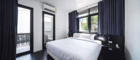 A modern hotel room with a large bed, a nightstand, a desk lamp, and a window with curtains.