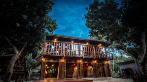 A wooden cabin with a balcony, surrounded by trees. - Nan De Panna Riverside Homestay (Phu Phiang)