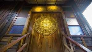 A wooden door with intricate carvings and a circular design in the center. - Nan De Panna Riverside Homestay (Phu Phiang)