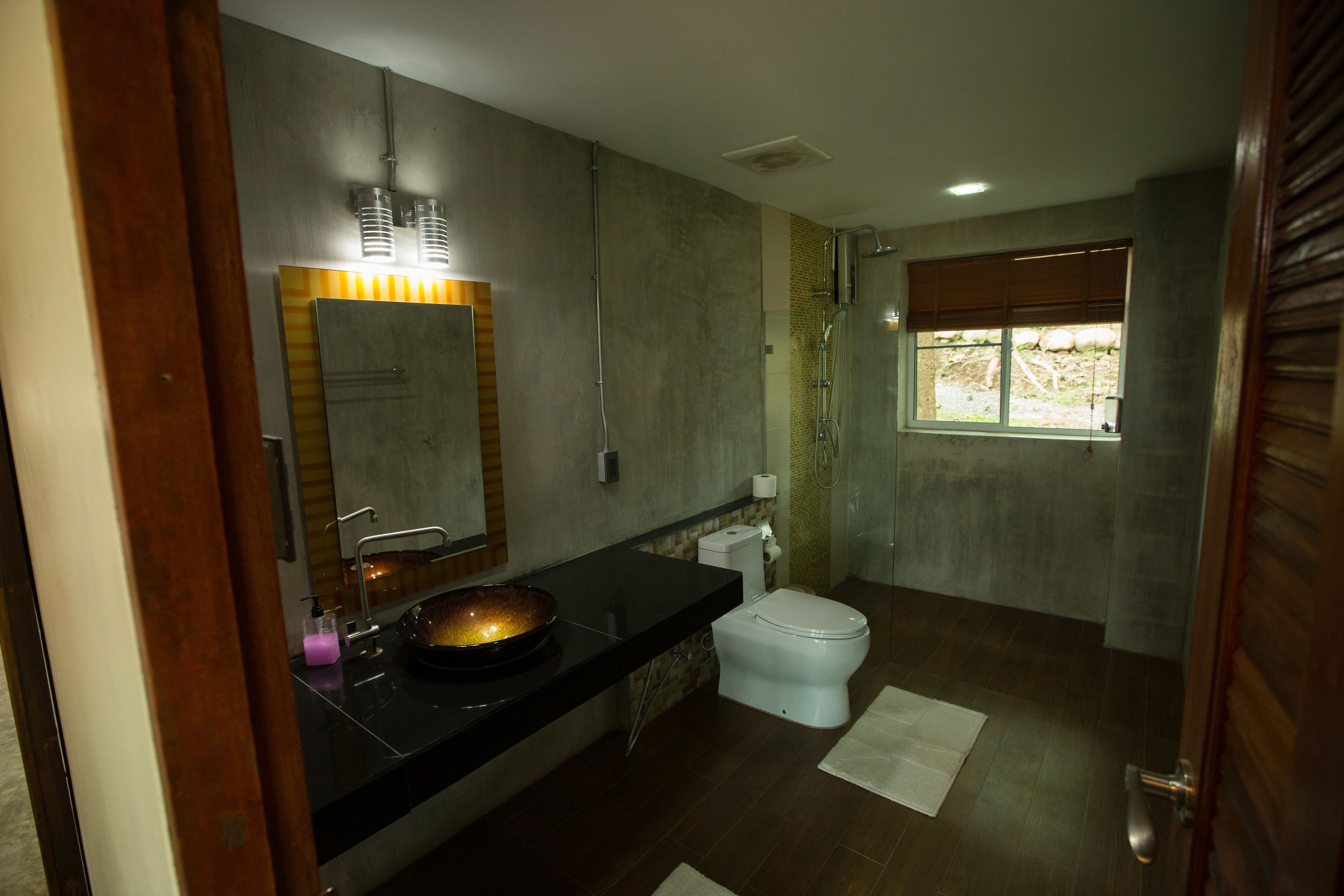 A modern bathroom with a black countertop, a large mirror, a white toilet, and a shower area.