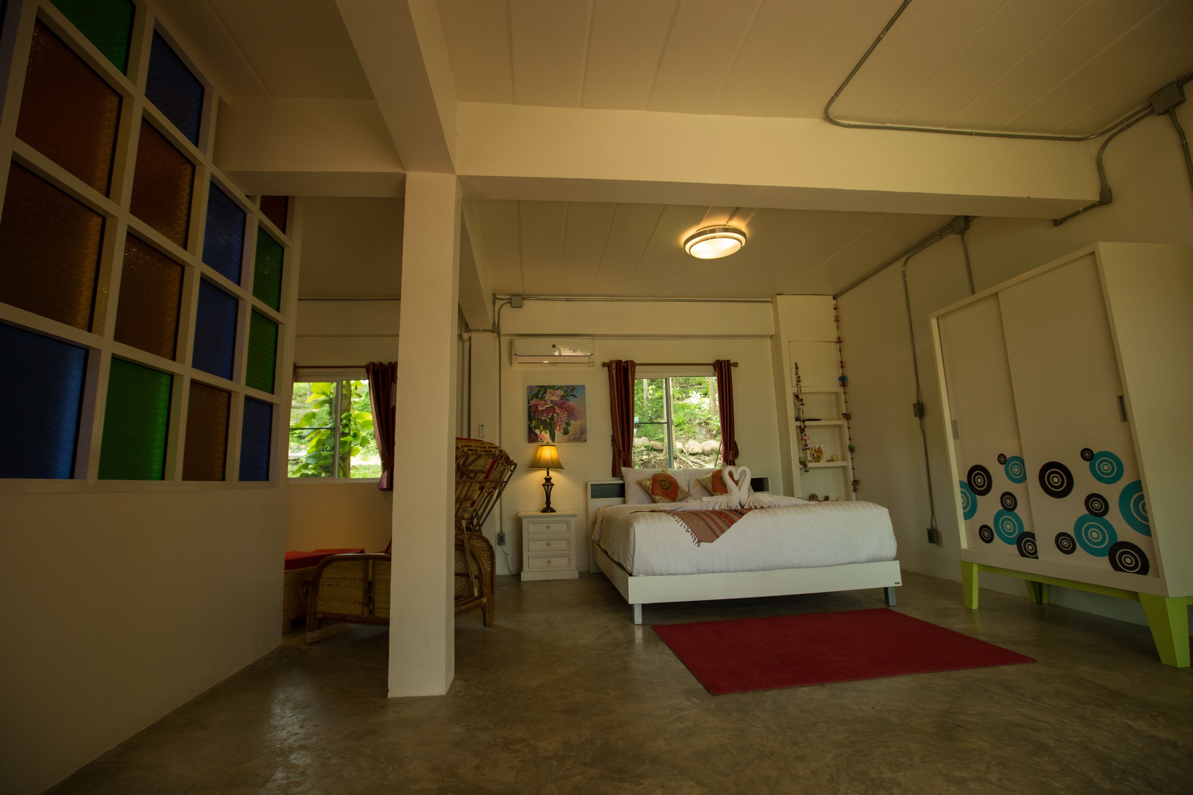 A bedroom with a bed, a nightstand, a lamp, a chair, and a window with curtains.
