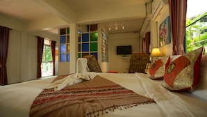 A hotel room with a large bed, a TV, a desk with a lamp, and a window with curtains. - Nan De Panna Riverside Homestay (Phu Phiang)