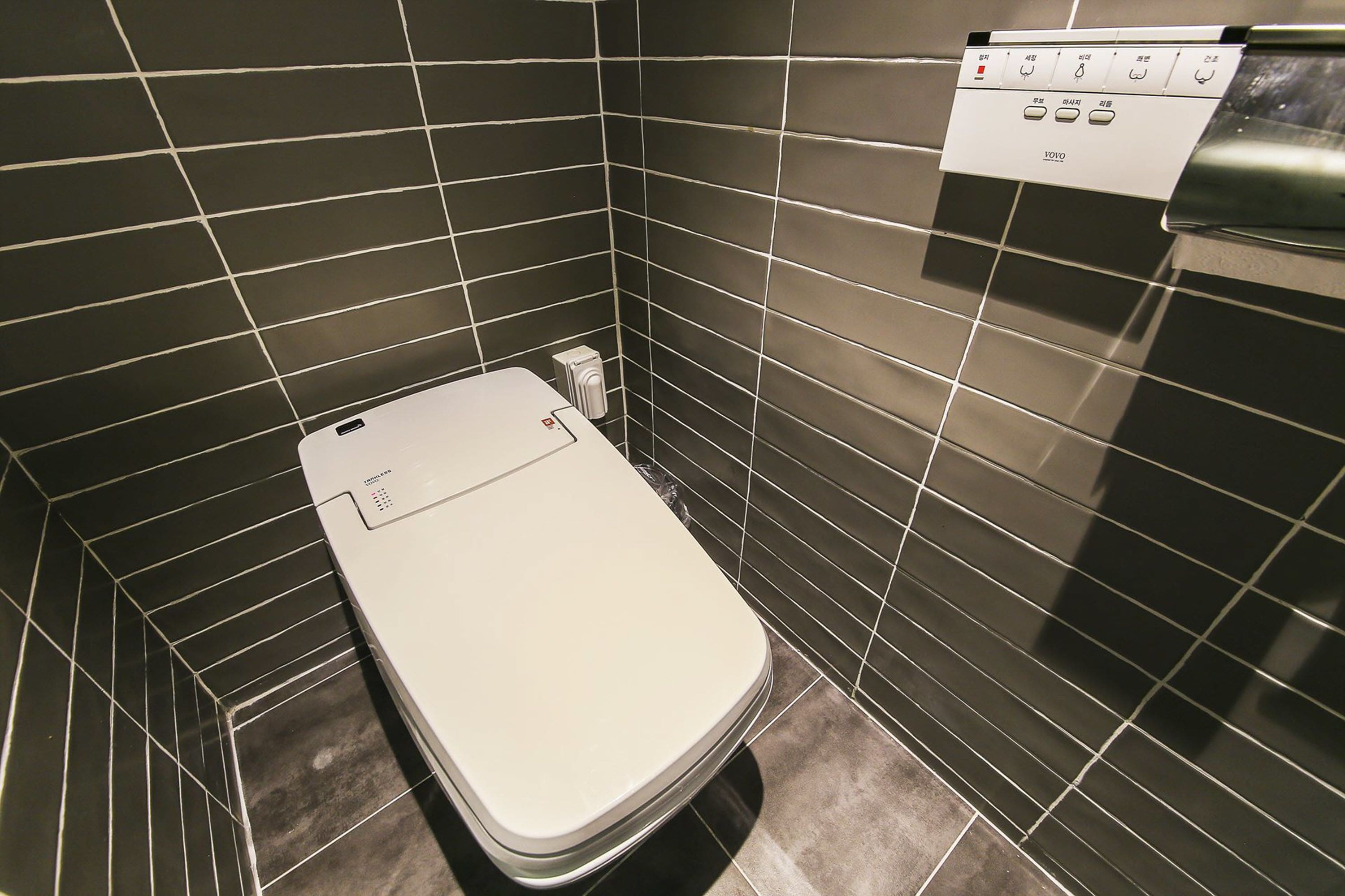 Ein kleines, modernes Badezimmer mit Toilette, Bedienfeld darüber und dunkel gefliesten Wänden.
