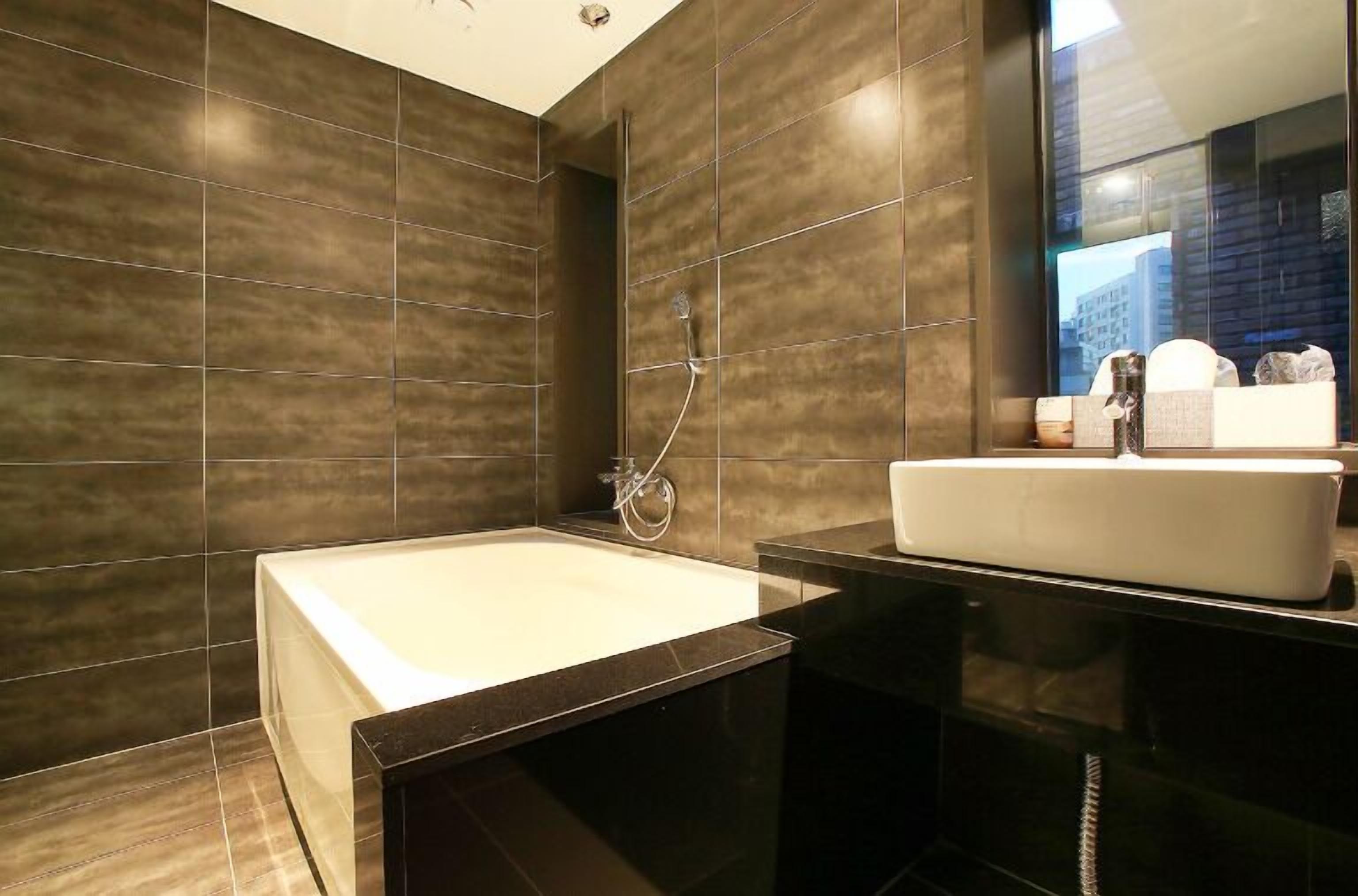 A modern bathroom with a large bathtub, a sleek vanity with a mirror, and dark tiled walls.