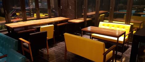 Een restaurantinterieur met houten tafels en gele zittingen met kussens.