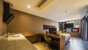 Hotelkamer met kitchenette, een bed, bureau met stoel, televisie en groot raam met gordijnen.