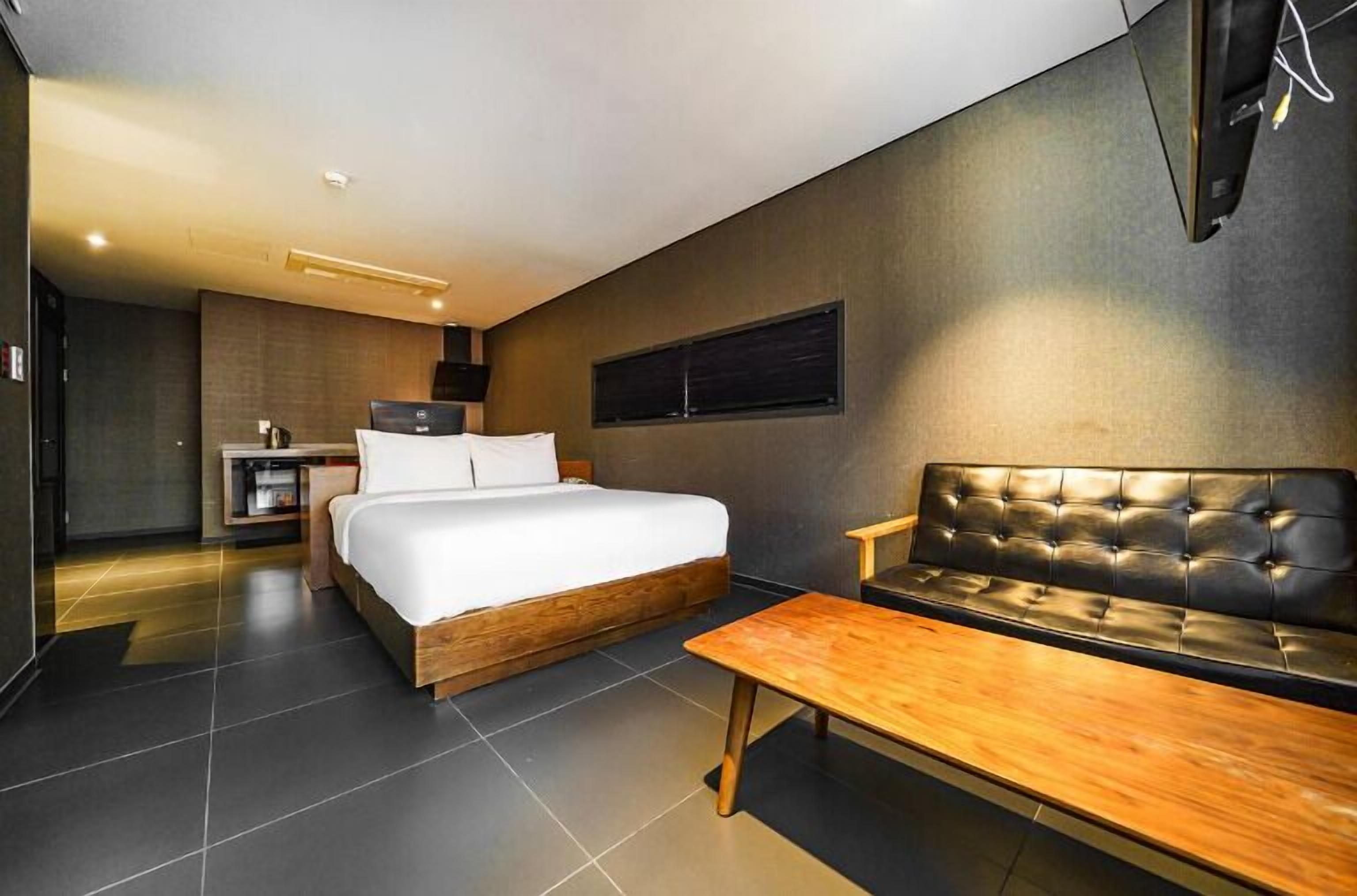 Una habitación de hotel moderna con una cama grande, un banco de madera y un televisor de pantalla plana montado en la pared.