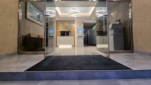 Un área de recepción moderna con puertas de vidrio, un mostrador de recepción y un quiosco informativo digital.