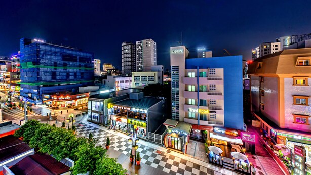 Un paisaje urbano nocturno con varios edificios, incluido un hotel que muestra un cartel con la leyenda 'Trevi Hotel'.