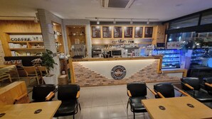 Interior de una cafetería con mostrador, carteles de menú, zona de estar y un letrero que dice 'Pick Up & Return'.