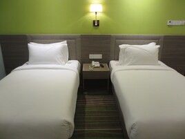 A hotel room with two single beds, a nightstand with a phone and a lamp, and a green wall.