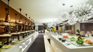 A modern hotel dining area with buffet-style food stations, contemporary lighting fixtures, and a clean, spacious layout. - Cosmo Hotel Kuala Lumpur (Kuala Lumpur)