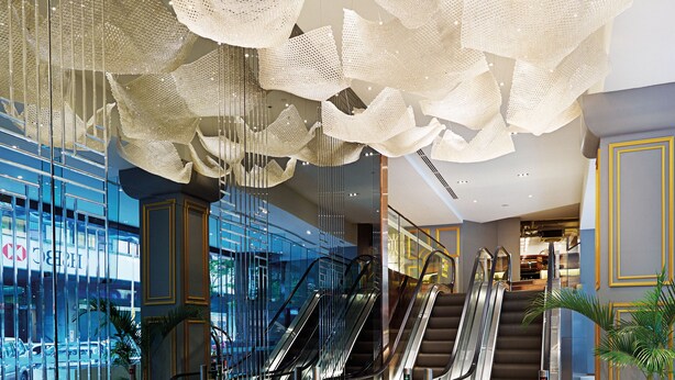A modern lobby with glass walls, escalators, and a decorative ceiling. - Cosmo Hotel Kuala Lumpur (Kuala Lumpur)