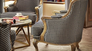 A room with two houndstooth patterned armchairs, a small table, and a bookshelf filled with books. - Cosmo Hotel Kuala Lumpur (Kuala Lumpur)