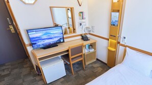 Hotelkamer met een bed, een bureau met een computer, een kleine koelkast, een nachtkastje met een lamp en een spiegel.