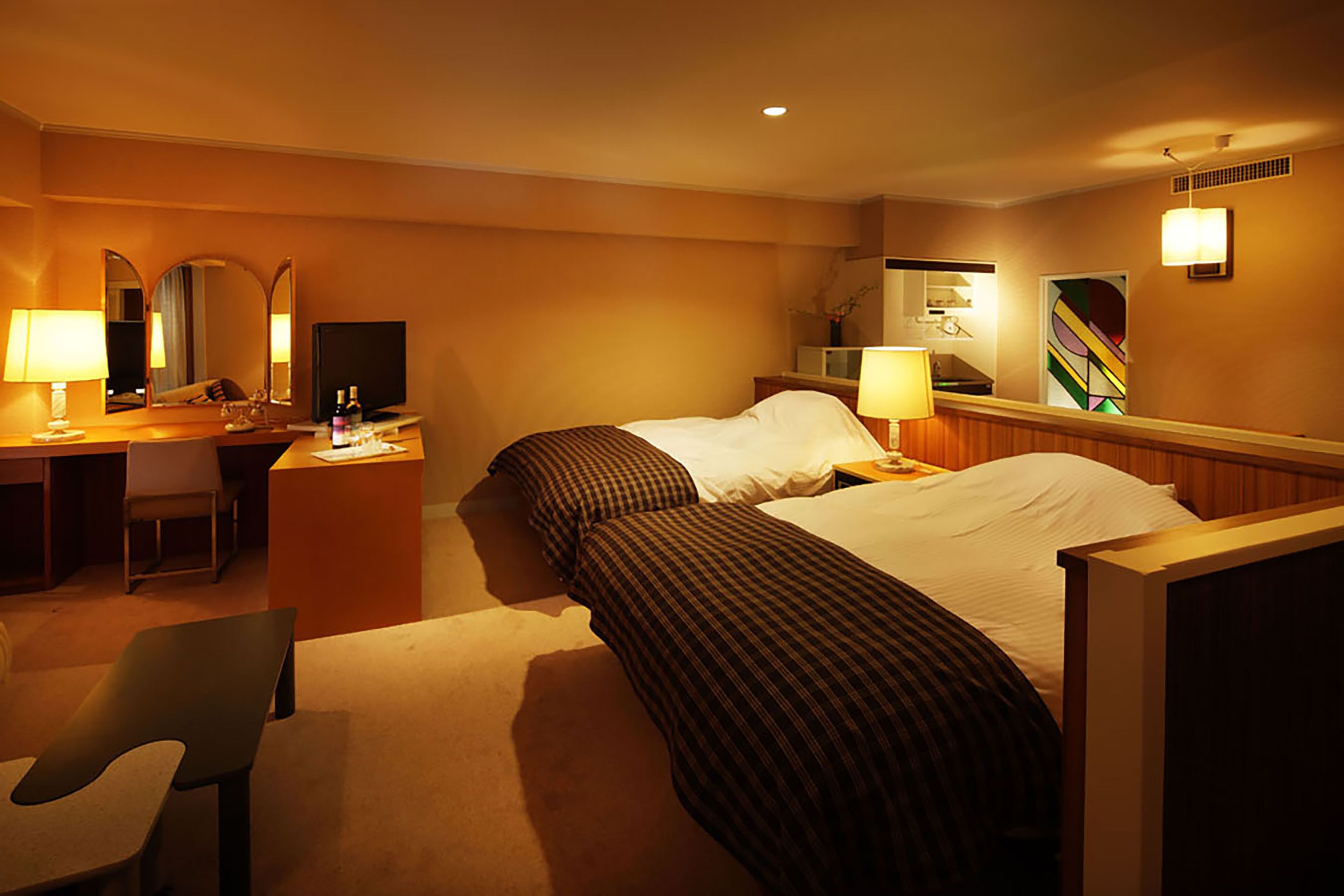 Ein Hotelzimmer mit zwei Betten, einem Schreibtisch, einem Stuhl, einem Fernseher und einem Spiegel.