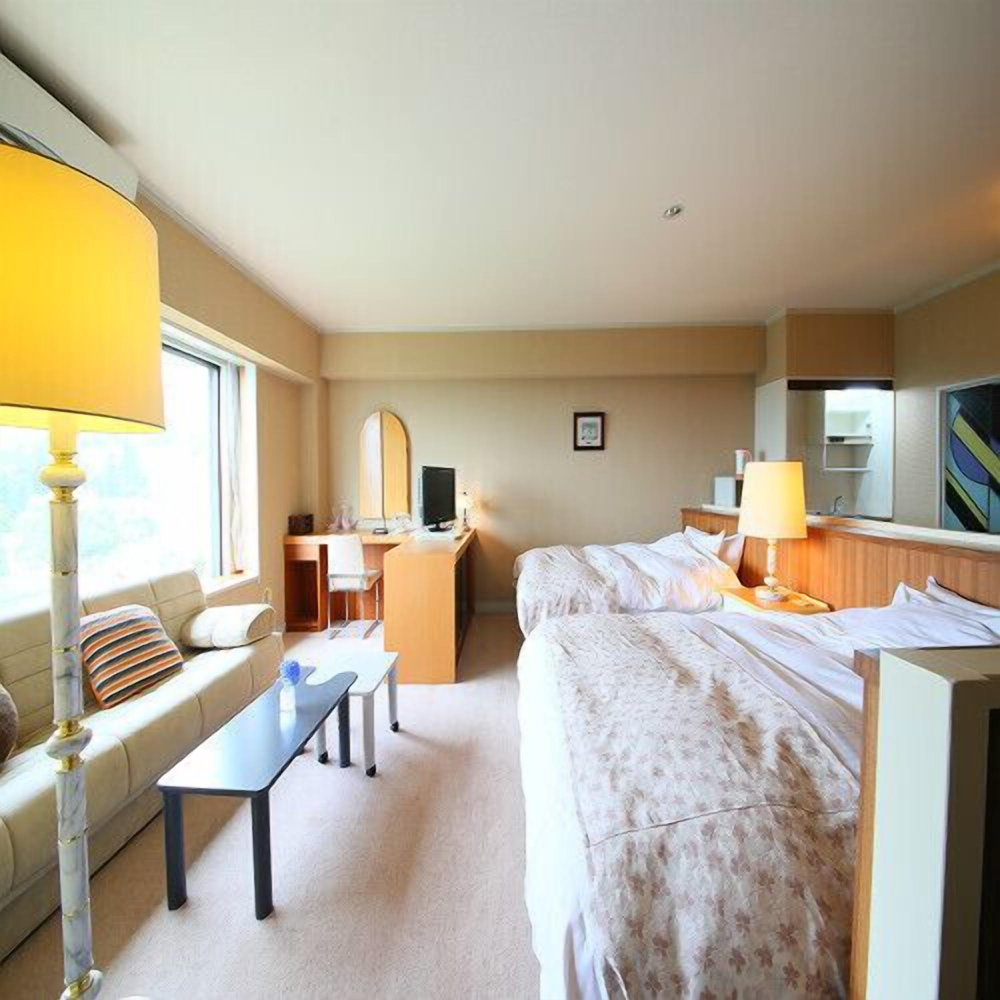 A hotel room with two beds, a desk, a chair, a lamp, and a window.