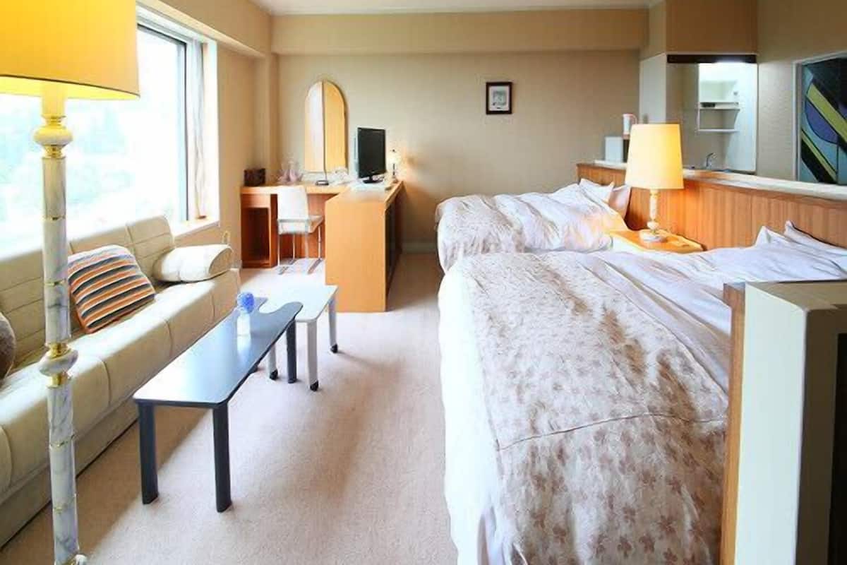 Une chambre d’hôtel avec deux lits, un bureau, une chaise, une lampe et une fenêtre.