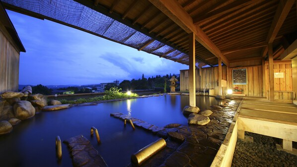 Un onsen japonés tradicional con estructura de madera, un sendero de piedra y vistas del paisaje circundante.