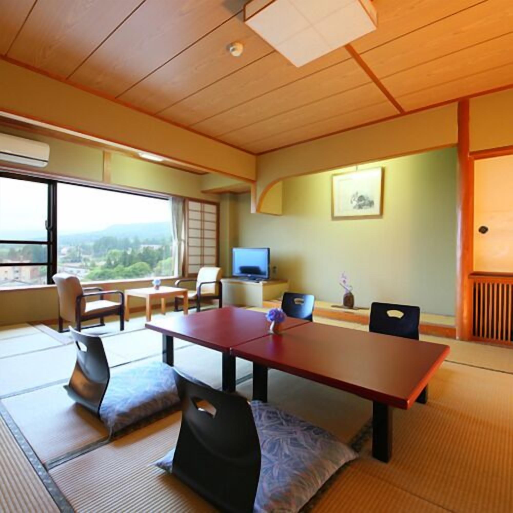 A traditional Japanese room with tatami flooring, a low table, chairs, a television, and a view of the outdoors.