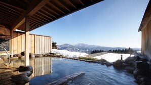 Un site de sources chaudes doté d’une terrasse en bois, d’escaliers en pierre et offrant une vue sur des montagnes enneigées.